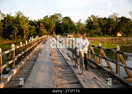 Homme local avec un vélo debout sur un vieux pont en bois dans l'île de majuli dans l'assam, en inde Banque D'Images