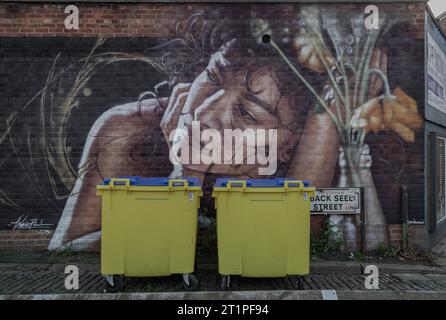 Liverpool, Royaume-Uni - Oct 09, 2023 - deux jaune Wheelie bin avant de Portrait graffiti spray peinture dessin sur le mur à Seel Street, espace pour le texte, S. Banque D'Images