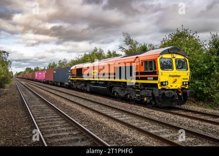 DERBY, ROYAUME-UNI - 6 OCTOBRE 2023. Un train de marchandises Freightliner intermodal de classe 66 avec caisse porte-conteneurs sur un chemin de fer principal peint dans la société mère Banque D'Images