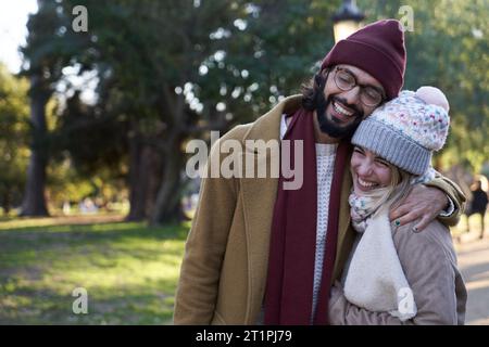 Couple heureux embrassé et rire ensemble tout en marchant à l'extérieur dans un parc pendant l'hiver. Banque D'Images