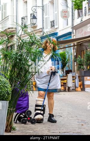 Femme dans la rue portant une botte de soutien médical post-opératoire et plâtre moulé - Loches, Indre-et-Loire (37), France. Banque D'Images