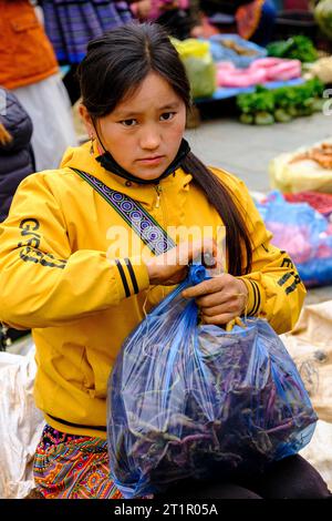 Bac Ha, Vietnam. Scène du marché du dimanche. Young Hmong Girl Wrapping achat dans un sac. Province de Lao Cai. Banque D'Images