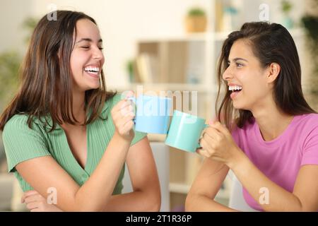 Deux amis heureux riant et grillant avec des tasses à la maison Banque D'Images