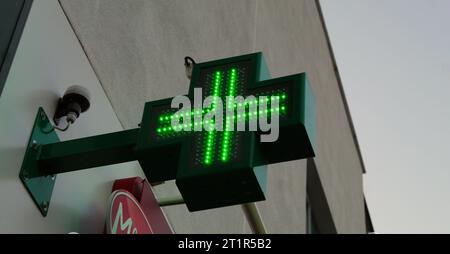 Photo d'une croix verte de pharmacie fixée à l'extérieur d'un mur blanc. Banque D'Images