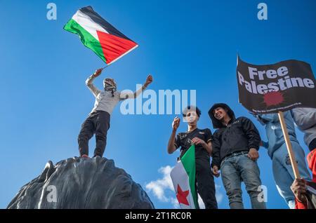 Londres, Royaume-Uni. 14 octobre 2023 : des manifestants pro-palestiniens se tiennent debout sur la statue du lion géant sur la place Trafalgar tenant un drapeau palestinien en soutien à Pal Banque D'Images