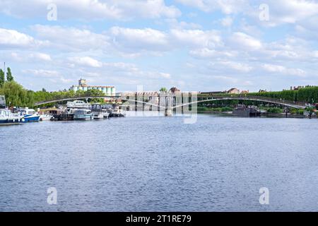 Auxerre, FRANCE - 16 juillet 2023 : passerelle au-dessus de l'Yonne et bateaux amarrés le long de la rive. Banque D'Images