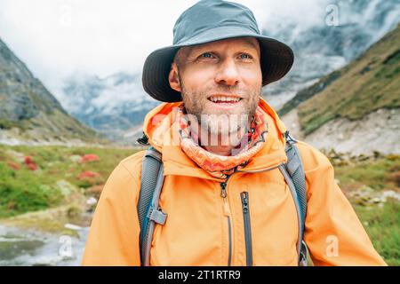 Portrait de Smiling Man avec sac à dos habillé veste imperméable orange et chapeau drôle marchant le chemin pendant le trek du parc national Makalu Barun au Népal. Banque D'Images