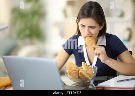 Glutton étudiant anxieux mangeant et étudiant en ligne à la maison Banque D'Images