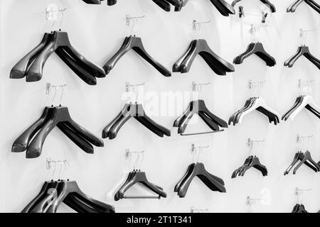 Cintres en plastique vides noirs assis sur un mur blanc dans un magasin, concept de vente Banque D'Images