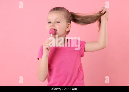 Mignon petite fille léchant sucette sur fond rose Banque D'Images