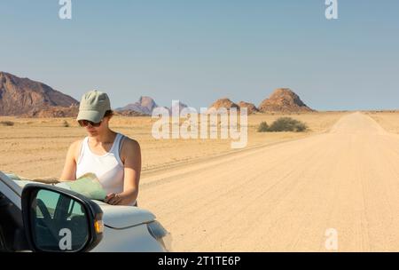 Jeune femme voyageur dans le chapeau regardant dans la carte touristique debout près de la voiture en afrique Banque D'Images