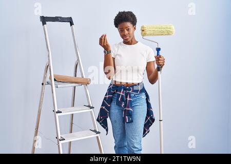 Femme afro-américaine tenant peintre à rouleaux faisant le geste italien avec la main et les doigts expression confiante Banque D'Images