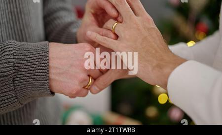 Couple de deux hommes célébrant noël mettant bague de mariage au doigt à la maison Banque D'Images