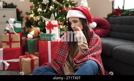 Belle femme hispanique portant un chapeau de noël avec une expression triste à la maison Banque D'Images