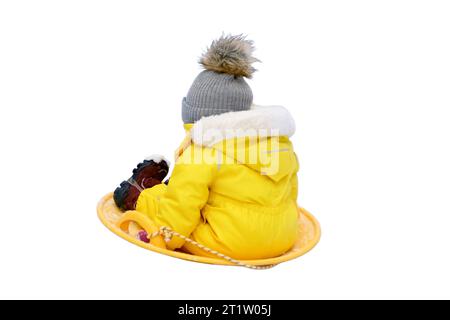 Bébé tout-petit heureux monte sur un traîneau à glace dans la neige dans une combinaison de neige jaune, isolé sur fond blanc. Enfant garçon en vêtements chauds marche dans le parc d'hiver Banque D'Images