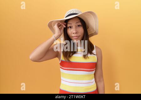 Femme chinoise d'âge moyen portant un chapeau d'été sur fond jaune inquiet et stressé au sujet d'un problème avec la main sur le front, nerveux et anxieux pour Banque D'Images