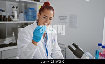 Brillante jeune femme rousse scientifique engrosée dans la recherche médicale, mesurant méticuleusement le liquide dans un tube à essai, gants de sécurité sur, à la h occupé Banque D'Images