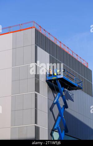 Travailleurs de la construction sur un ascenseur à ciseaux fixant le revêtement à un bâtiment, Glasgow, Écosse, Royaume-Uni, Europe Banque D'Images