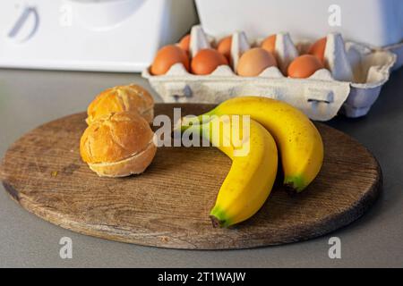 branche de bananes se trouve sur la table avec des œufs et des pains à hamburger. Banque D'Images
