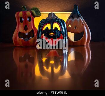 Trois petites et drôles fausses citrouilles Halloween avec différentes expressions faciales. Décorations placées sur une surface en bois avec un fond noir. Banque D'Images