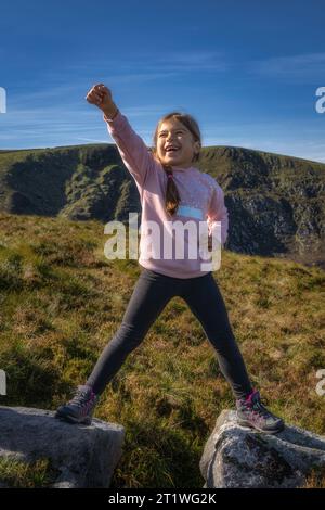 Jeune fille debout en fente sur deux rochers avec la main levée dans le triomphe et la victoire alors qu'elle gravissait la montagne. Randonnée en famille dans les montagnes de Wicklow, Irlande Banque D'Images