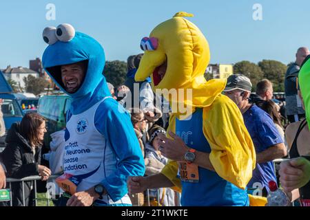 Great South Run, 15 octobre 2023, Portsmouth, Hampshire, Angleterre, ROYAUME-UNI. Des milliers de concurrents ont couru dans le 10 Mile Great South Run qui a commencé et s'est terminé à Southsea, Portsmouth. En plus des coureurs d'élite, beaucoup d'autres personnes ont participé à la course pour la charité ou pour leurs clubs. Sur la photo : deux hommes vêtus de muppet montrent costume de robe fantaisie, le monstre de cookie et les costumes de grand oiseau Banque D'Images