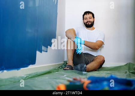 rénovation domiciliaire. Homme barbu caucasien ayant le repos après avoir peint l'image du mur avec la mise au point sélective Banque D'Images