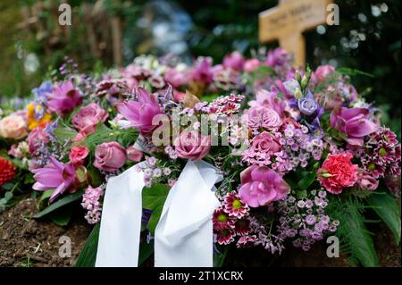 couronne funéraire sur une tombe avec des rubans blancs et des fleurs dans des tons roses avec une croix en bois dans un fond flou Banque D'Images