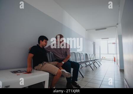 Un enfant et son grand-père attendent leur tour à l'hôpital. Ils sont assis sur un banc dans la salle et ont une conversation. Banque D'Images