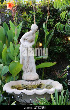 Belle statue d'une femme versant de l'eau d'un vase dans une fontaine dans un cadre de jardin romantique. Banque D'Images