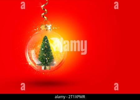 Arbre de Noël avec des lumières à l'intérieur d'une boule transparente accrochée à un ruban d'or. Fond rouge du nouvel an avec décor de Noël, bokeh Banque D'Images