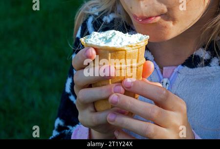 fille léchant la crème glacée à la pistache dans une tasse à gaufres avec sa langue par une journée ensoleillée: Banque D'Images