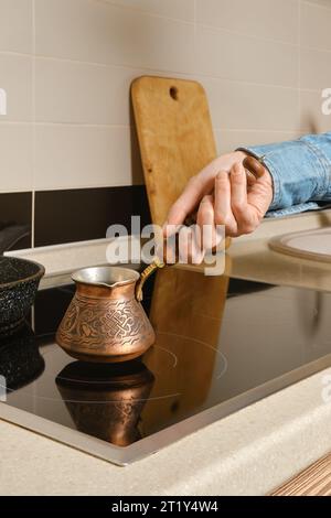 Main femelle mettre la cafetière turk sur la cuisinière électrique Banque D'Images