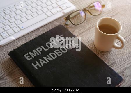 Image rapprochée du livre avec le texte EMPLOYÉ MANUEL entouré par une tasse de café et des verres sur le bureau Banque D'Images