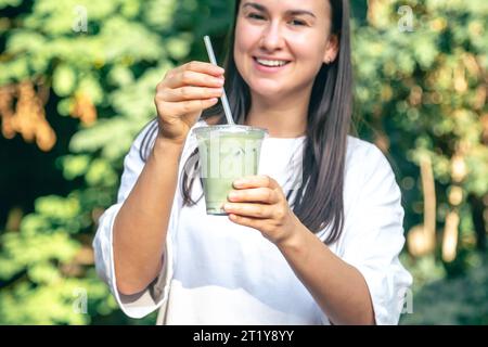 Femme élégante buvant du matcha latte dans le parc. Banque D'Images