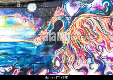 Graffiti en bord de mer sur une digue à Herne Bay sous la forme d'une peinture très détaillée d'un dragon crachant de feu au bord de la mer avec des lunes blanches ou des soleils au-dessus. Peint par une jeune femme inconnue. Le tableau fait partie d'une série liée par un horizon commun le long du mur. Banque D'Images