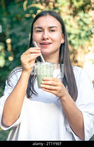 Femme élégante buvant du matcha latte dans le parc. Banque D'Images