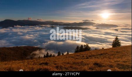 Coucher de soleil caché derrière les nuages et brouillard sur les collines, soleil jaune vif sur un paysage nuageux coloré, ciel bleu violet orange. Banque D'Images