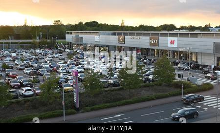 Voitures garées dans un parking près d'un centre commercial au coucher du soleil. Banque D'Images