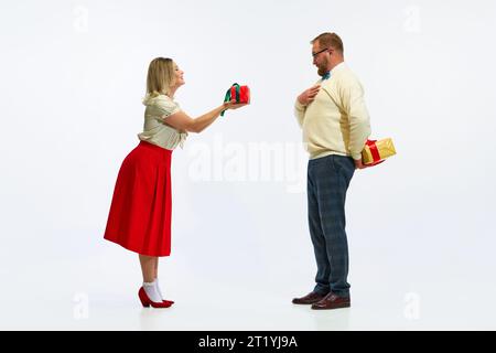 Joyeuses vacances d'hiver. Heureux, joyeux couple, tenue de mode rétro habillée sur fond blanc. Charmante femme a donné cadeau pour homme surpris Banque D'Images