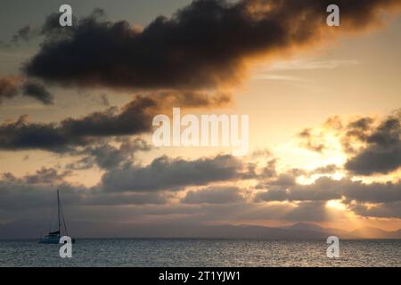 Un bateau flotte sur les eaux calmes des Caraïbes alors que le soleil se couche à l’horizon. Banque D'Images