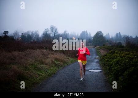 Un coureur travaille sur un sentier lors d'une soirée brumeuse dans un parc de la ville. Banque D'Images