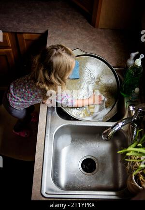 Petite fille laver la vaisselle dans l'évier de cuisine avec des bubles Banque D'Images