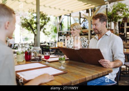 Famille avec bébé et fille lisant des menus dans un restaurant, choisissant la nourriture, les boissons. Dîner familial au restaurant. Banque D'Images