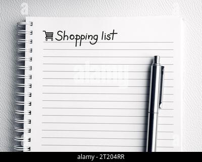 Liste d'achats, texte de note manuscrite sur la page vide du carnet. Modèle de feuille de papier blanc avec ligne et icône de panier sur le bloc-notes en spirale avec un silv Banque D'Images