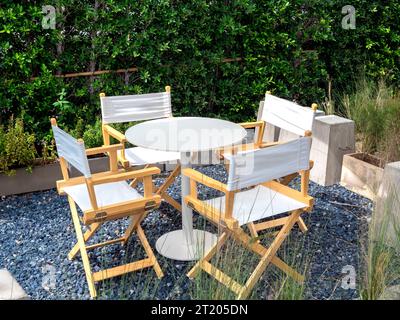 Quatre chaises de directeur vides, tissus et matériaux en bois avec table de forme ronde au jardin extérieur sur sol en pierre de gravier bleu sur arbre vert, brousse backgrou Banque D'Images