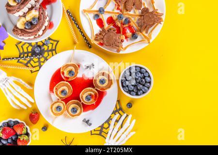 Petit déjeuner drôle pour les enfants pour Halloween. Crêpes sucrées maison créatives sous forme de monstres et symboles traditionnels d'Halloween, avec baies fraîches, chocolat Banque D'Images