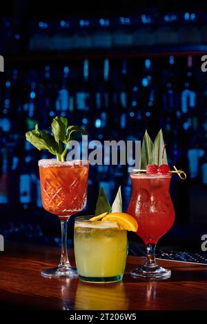 trois cocktails rafraîchissants avec des décorations de fruits et de plantes avec bar sur fond, concept Banque D'Images