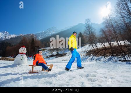 Père tirant en montée un garçon sur le traîneau en bois dans les montagnes Banque D'Images