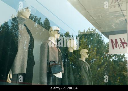 Bucarest, Roumanie - 15 octobre 2023 : vitrine du magasin H et M avec des vêtements de femmes de collection d'automne sur des mannequins et des arbres en plein air reflétés sur g Banque D'Images